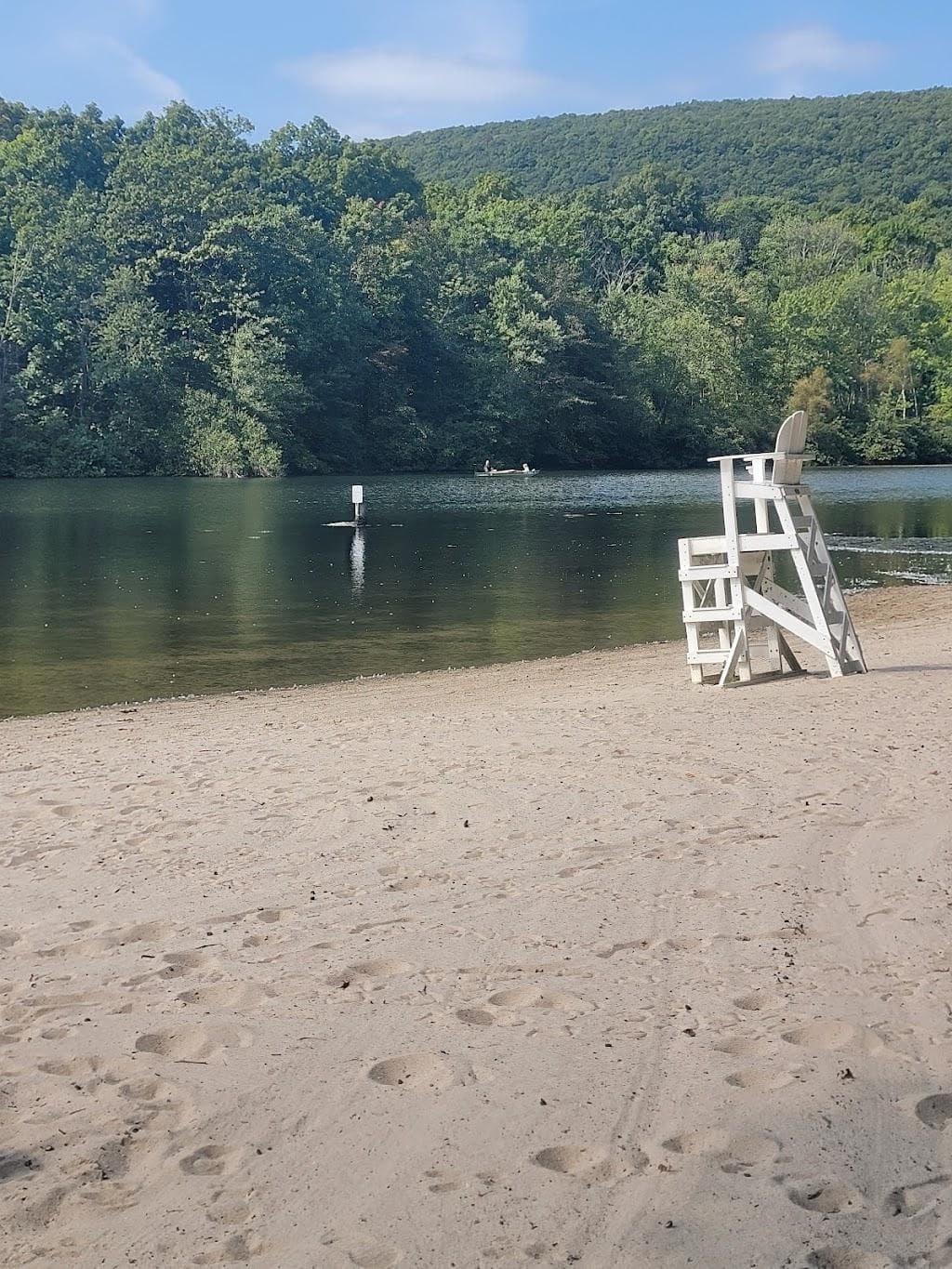 An empty white lifeguard stand on a sandy lake beach, with wooded hills behind the water.