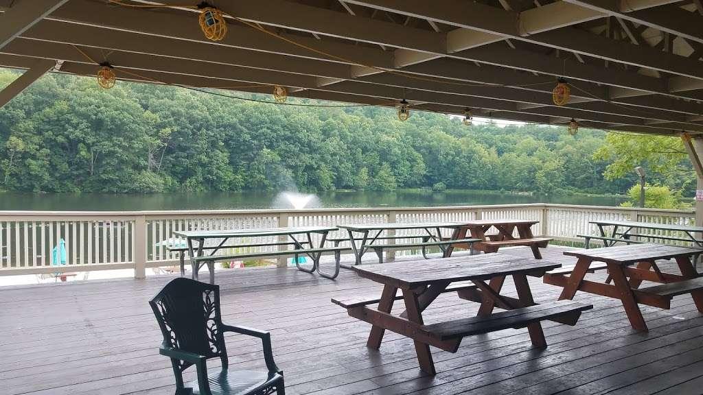 A covered wooden pavilion with picnic tables overlooking a lake and green hills.